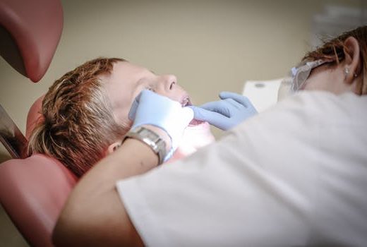 Dentists in Glasgow City centre wearing rubber gloves look into little boys mouth as he lies on the dental chair.